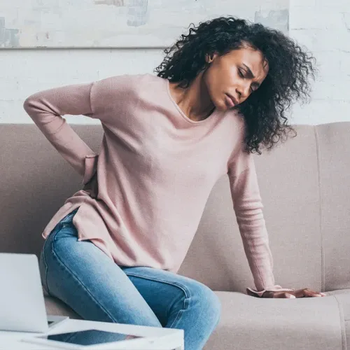 Woman on sofa experiencing lower back pain with a pained expression